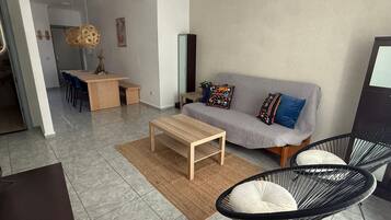 A modern living room with a sofa, a coffee table, a dining area with chairs, and a black chair with a cushion.