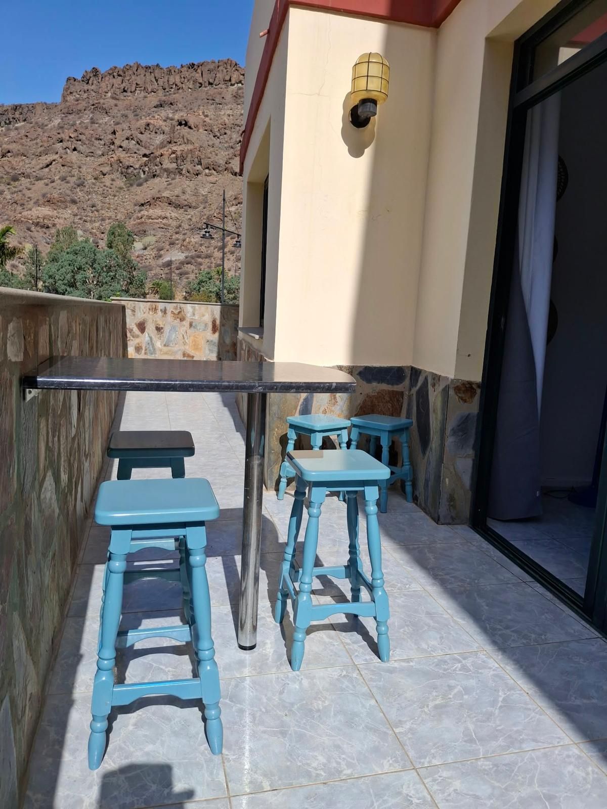 Un patio con una mesa, dos taburetes, un muro de piedra y vistas a la montaña.