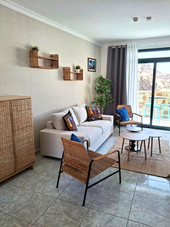 A living room with a sofa, two wicker chairs, a small table, and a potted plant.
