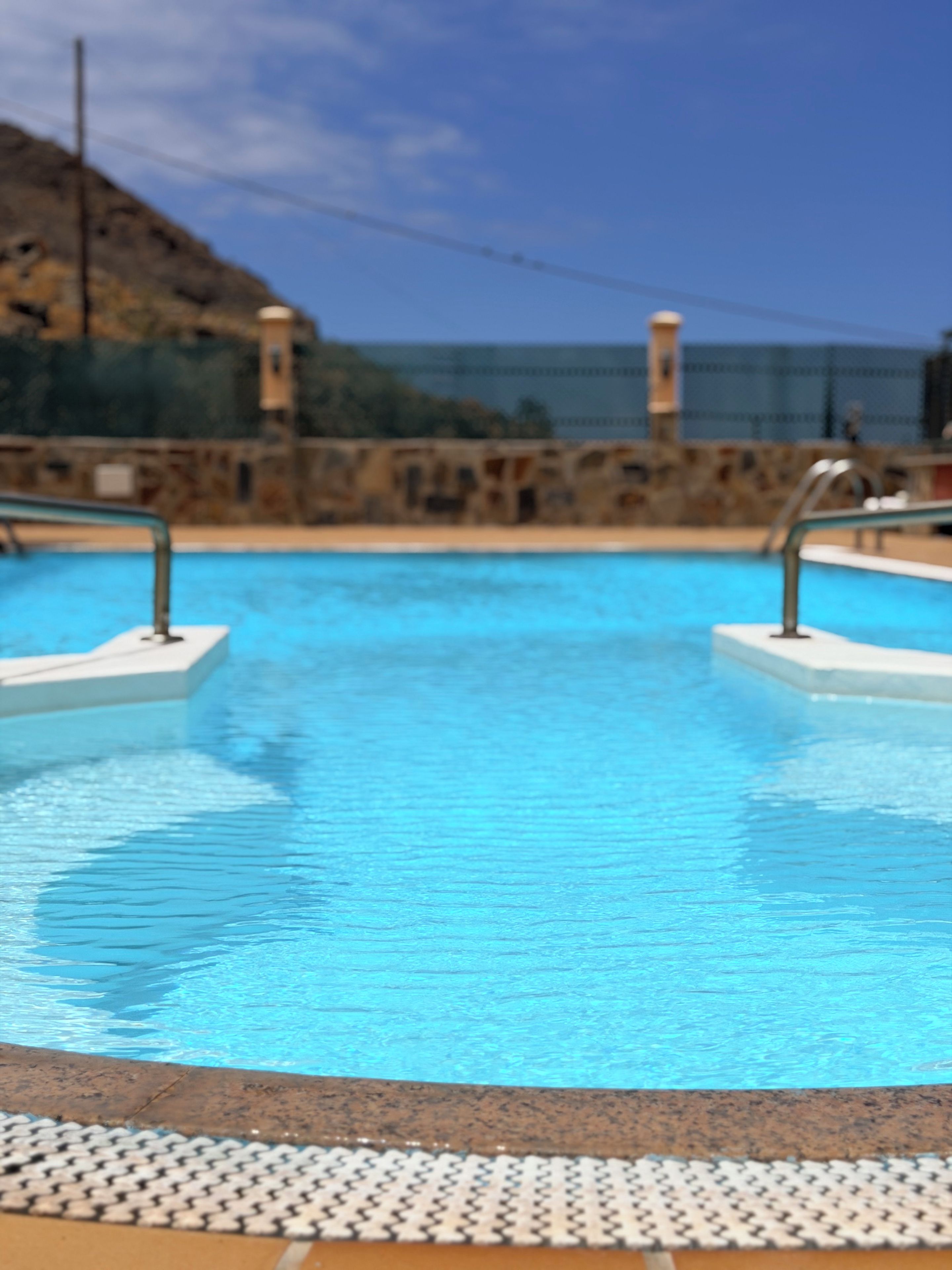 Ein Schwimmbecken mit klarem, blauem Wasser, umgeben von einer Steinmauer und Metallgeländern.