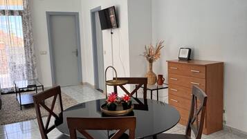 Comedor con una mesa redonda, cuatro sillas de madera, una mesita auxiliar con un florero y un televisor montado en la pared.