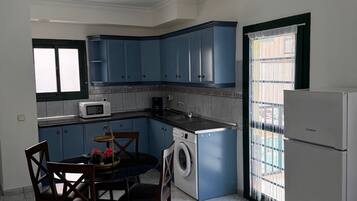 Cocina compacta con armarios azules, lavadora, microondas y un comedor con sillas y mesa.