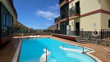 Una piscina con borde de baldosas, rodeada de edificios con balcones y un cielo despejado.