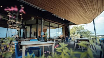 Un espace extérieur aménagé avec des tables et des chaises en bois, une paroi en verre et une vue sur l’extérieur.