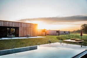 Un edificio moderno con una amplia entrada de vidrio, asientos al aire libre y una piscina reflectante.
