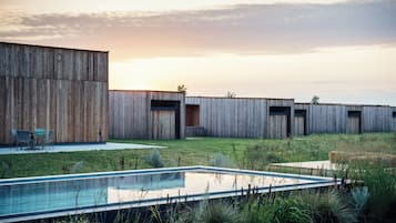 A modern building with a pool, surrounded by a grassy area and wooden structures.