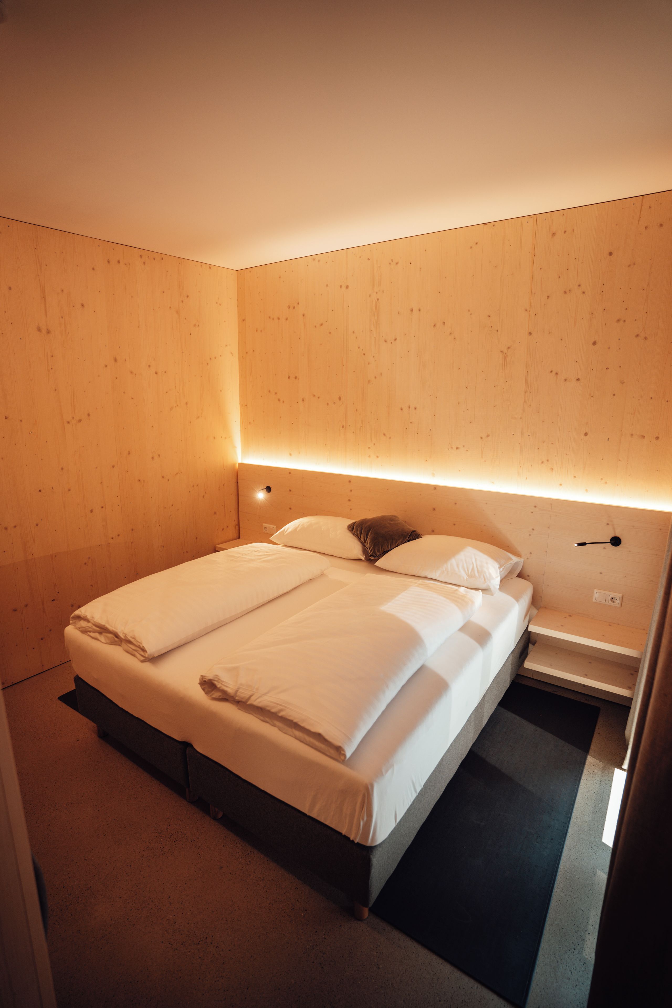 A hotel room with a wooden headboard, a bed with white linens, a bedside table, and a nightstand.