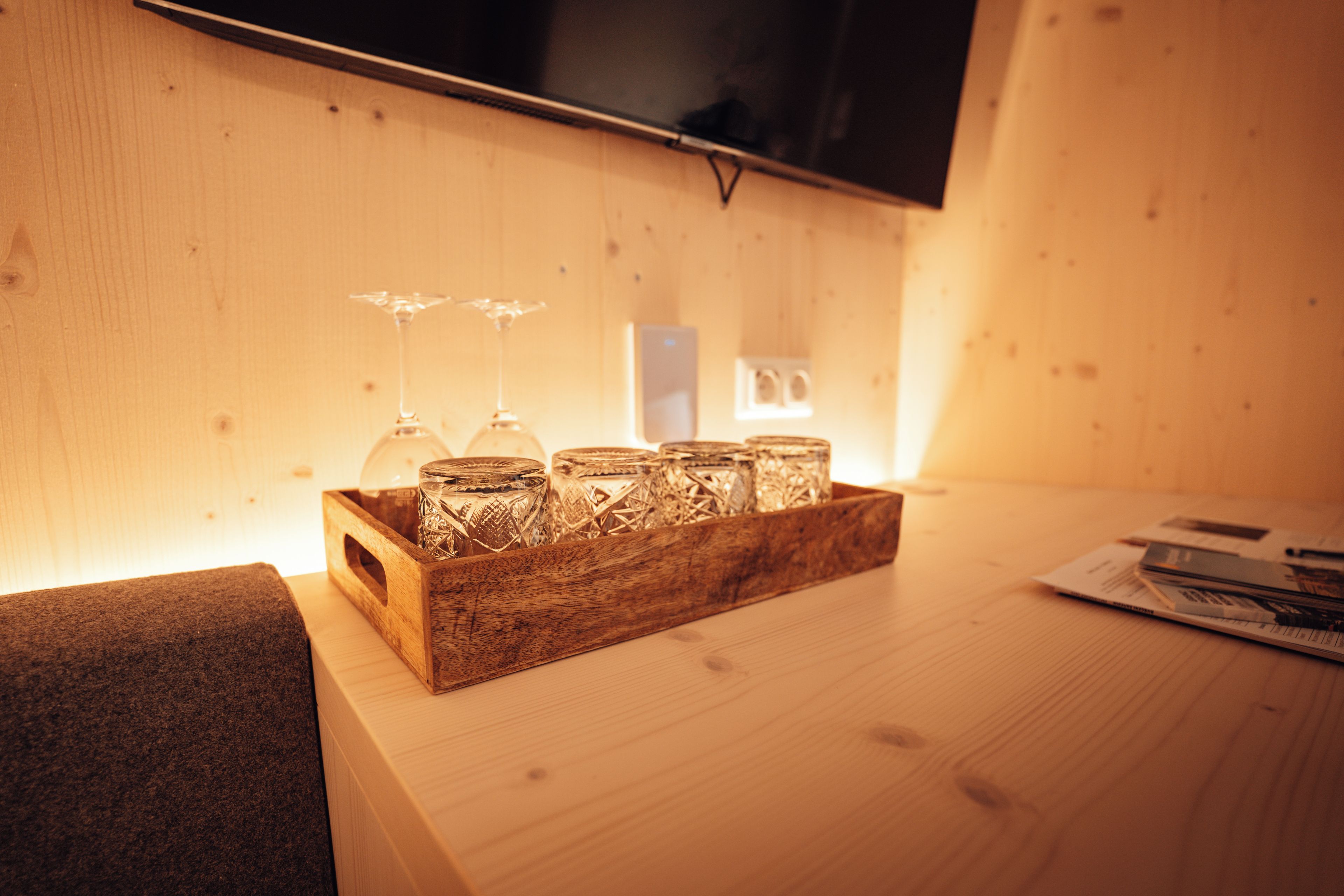A wooden tray with glassware on a table, a television mounted on the wall, and a wooden floor.