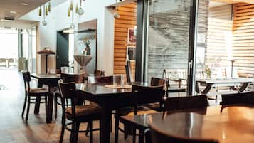 A modern restaurant interior with wooden tables and chairs, pendant lighting, and large windows.