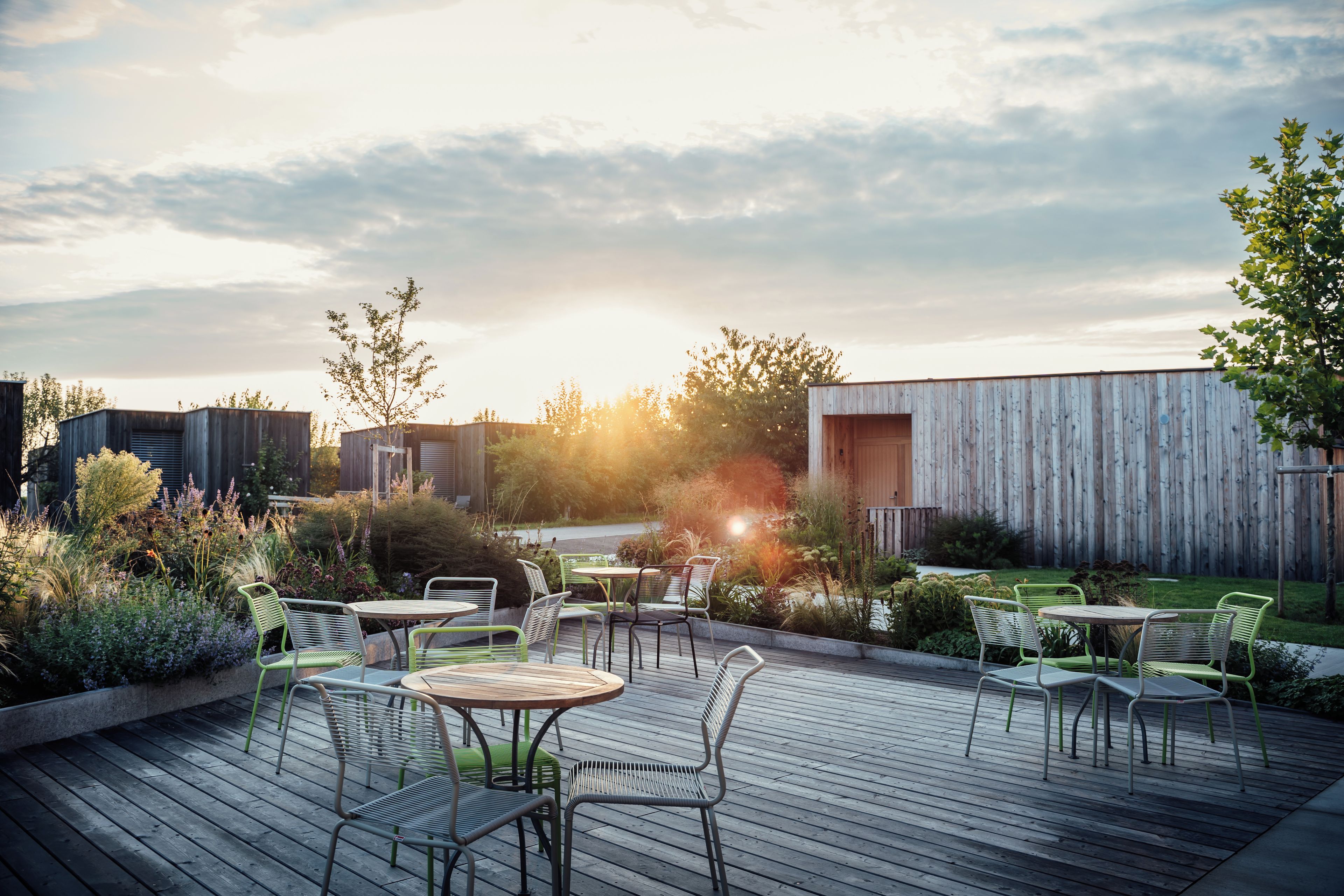 Eine Terrassengaststätte mit Metallstühlen und -tischen, umgeben von viel Grün und einem Holzzaun.