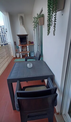 Un balcon avec une table et des chaises, un barbecue et des plantes en pot.