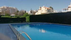 A rectangular swimming pool with a metal ladder on one side, surrounded by a low hedge and a paved deck. - Sulaosol Apartment with Shared Pool, Wi-Fi, and Air Conditioning (Portimão)