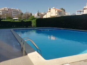 Une piscine rectangulaire avec un escalier en métal sur un de ses côtés, entourée d’une haie basse et d’une terrasse dallée.