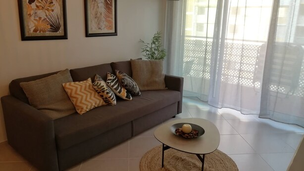 A living room with a sofa, decorative pillows, a coffee table, and two framed artworks on the wall. - Sulaosol Apartment with Shared Pool, Wi-Fi, and Air Conditioning (Portimão)