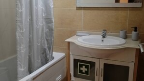 A bathroom with a bathtub, a sink, a mirror, and a cabinet with a medical symbol. - Sulaosol Apartment with Shared Pool, Wi-Fi, and Air Conditioning (Portimão)