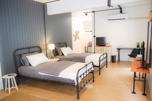 Ein Zimmer mit zwei Betten, einem Schreibtisch, einem Stuhl, einem Fernseher und einem kleinen Hocker.