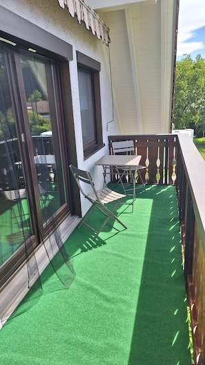 Ein Balkon mit einem grünen Rasenteppichboden, einem Tisch und zwei Stühlen.