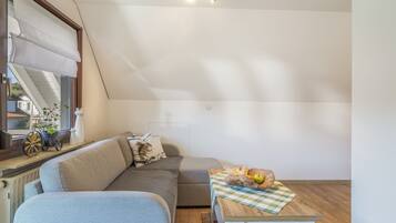 A cozy room with a sloped ceiling, a sofa, a small table with fruits, and a window with blinds.
