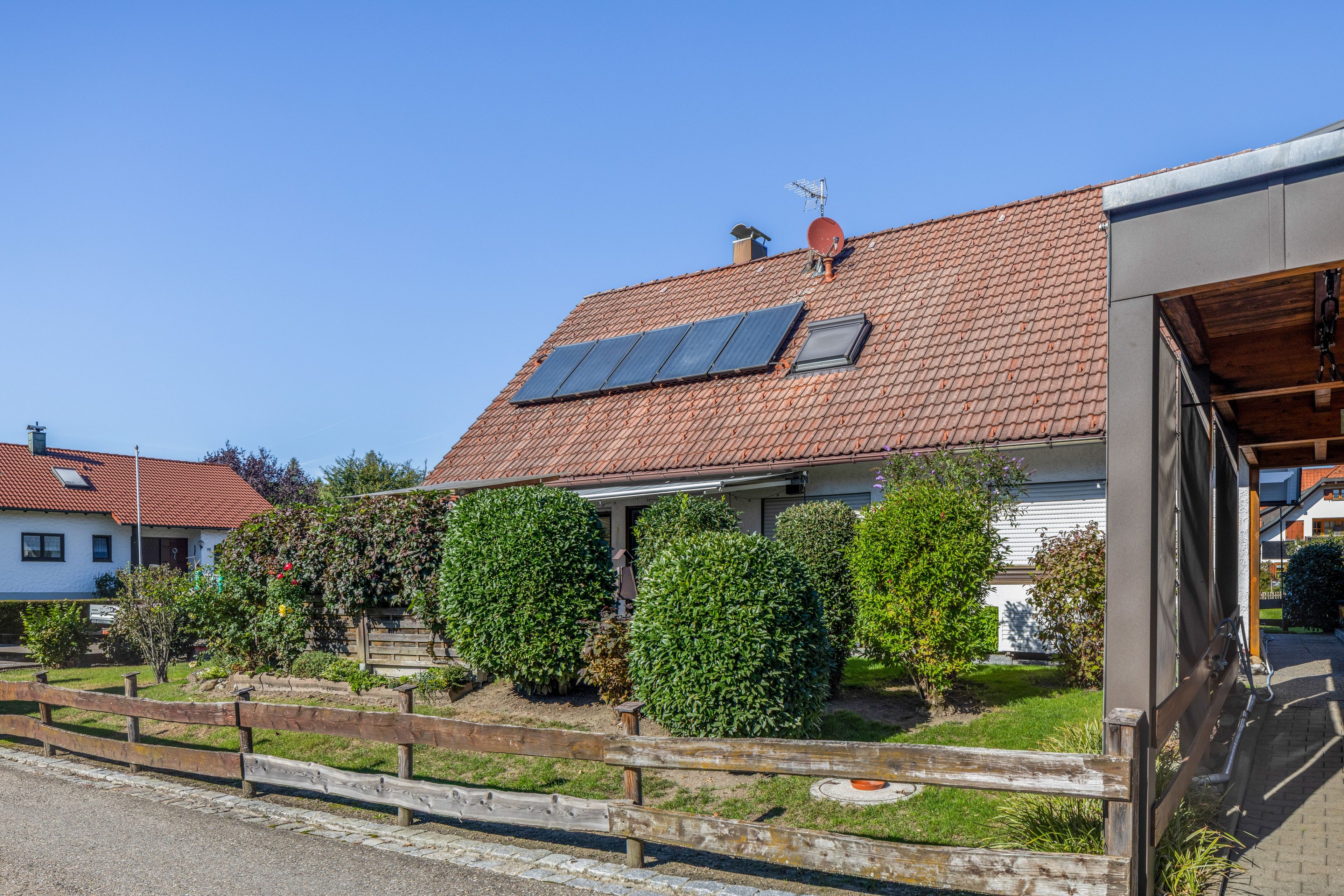 A residential building with a red-tiled roof, solar panels, and a wooden fence.