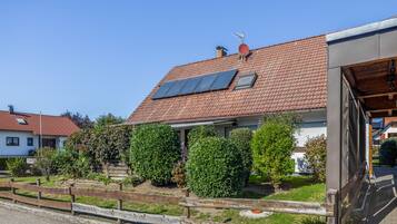 A residential building with a red-tiled roof, solar panels, and a wooden fence.