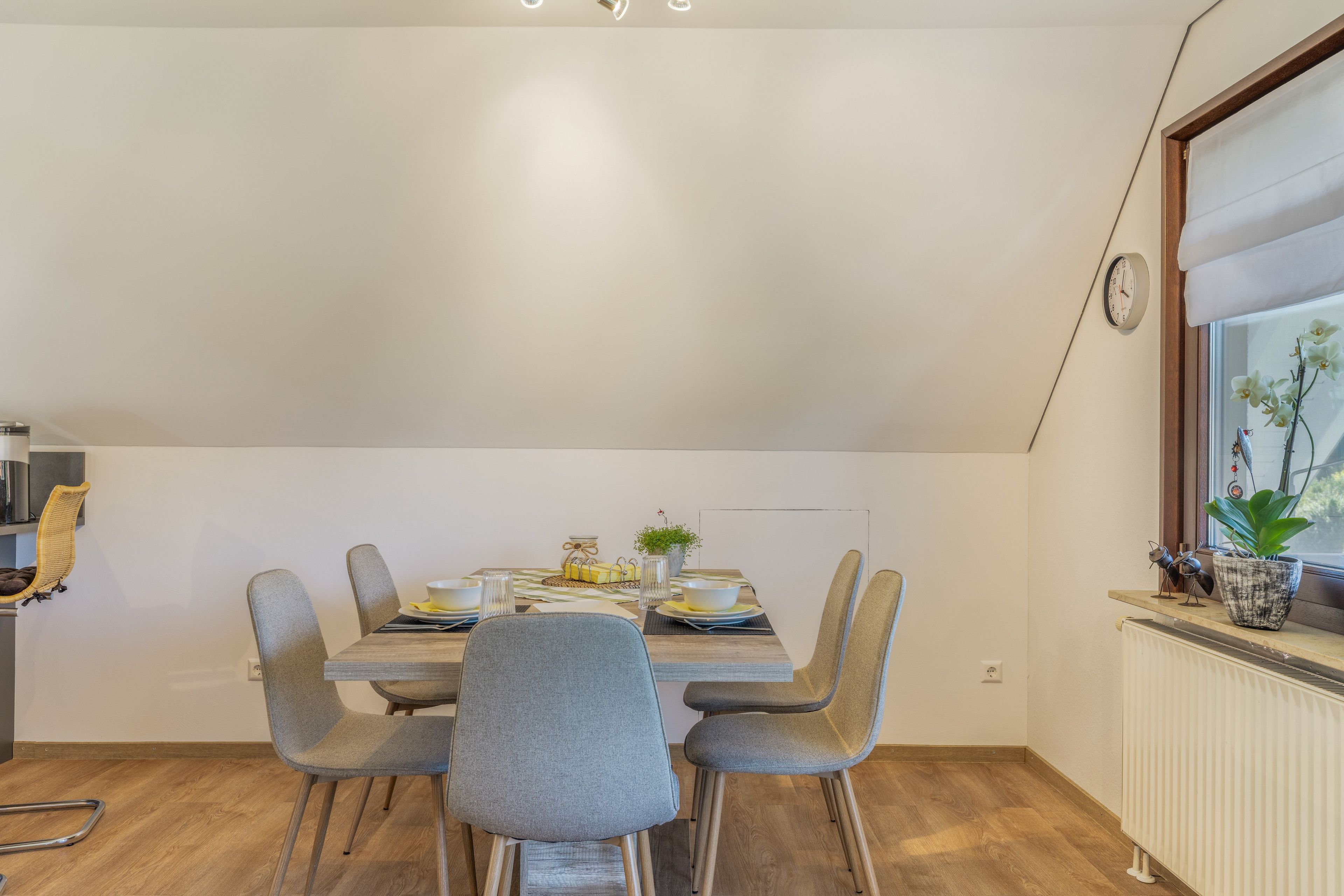 A dining area with a table set for four, surrounded by grey upholstered chairs.