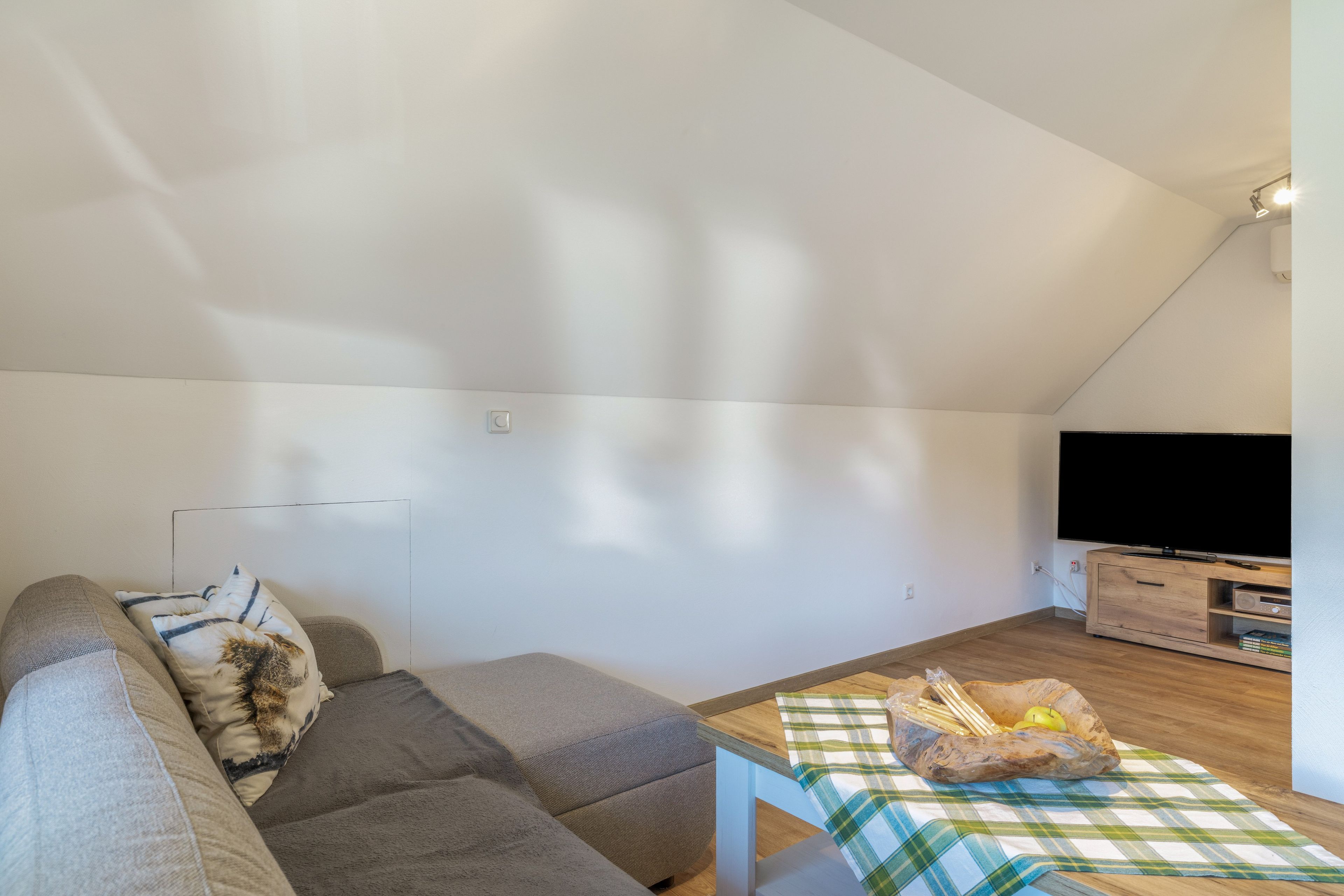 A modern living room with a sofa, a television, and a wooden coffee table with a plaid tablecloth.