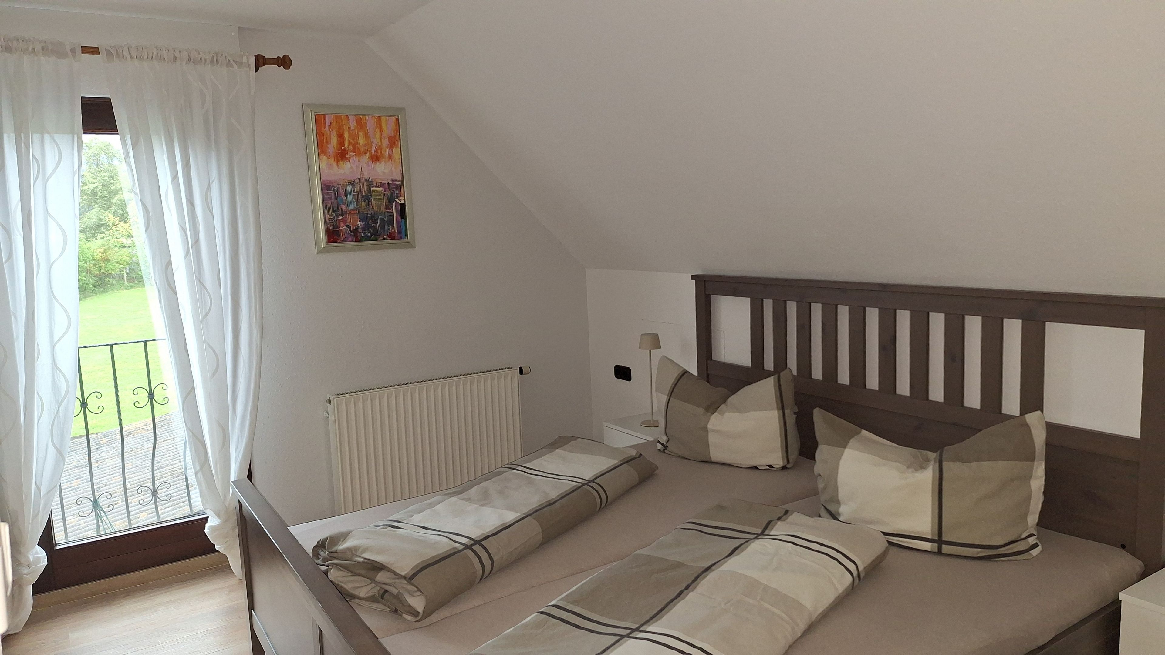 A bedroom with a bed, a radiator, a window with curtains, and a painting on the wall.