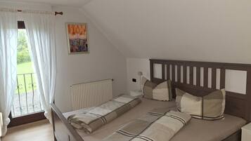 A bedroom with a bed, a radiator, a window with curtains, and a painting on the wall.
