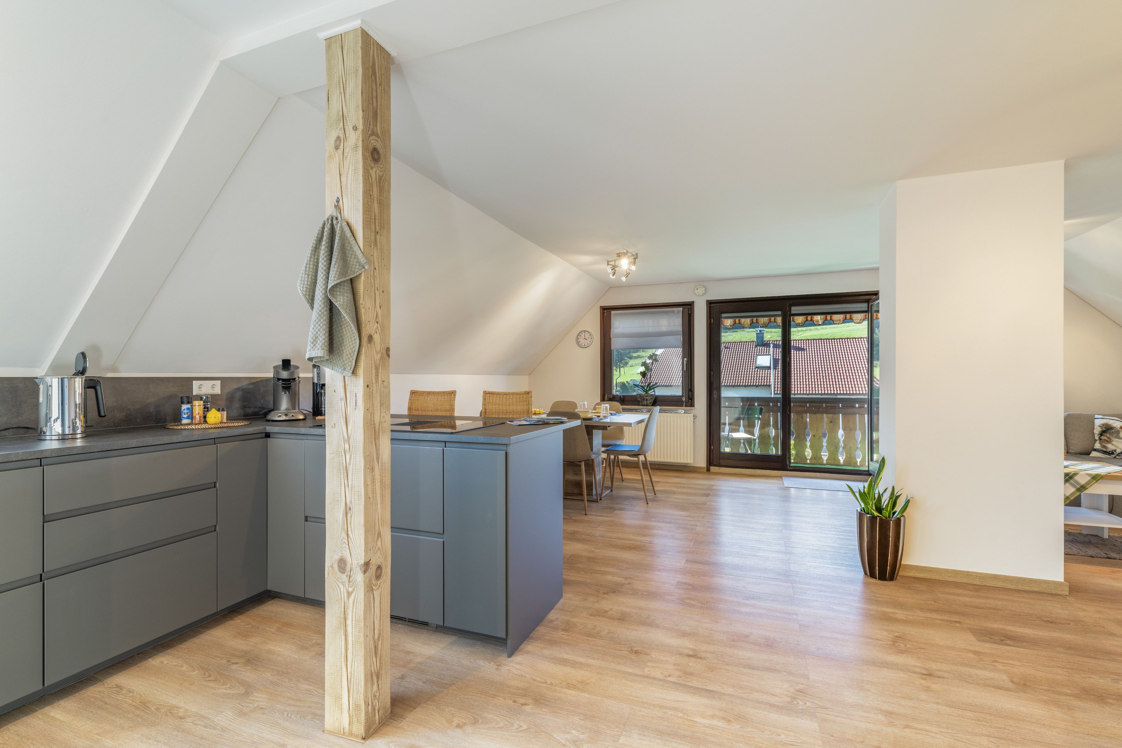 A modern kitchen with grey cabinets, a wooden column, and a dining area with a view of the outside.