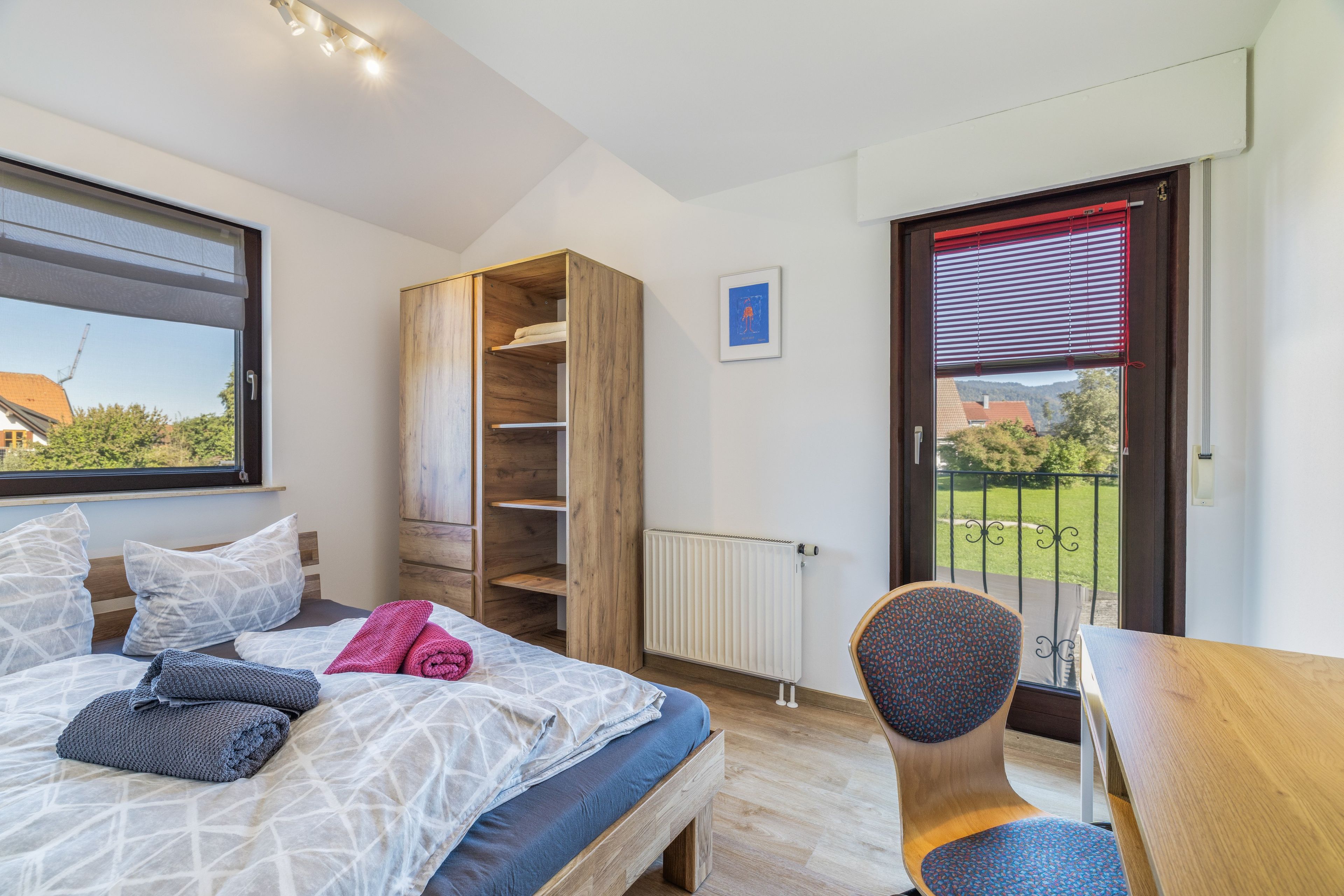 A bedroom with a bed, a wardrobe, a chair, and a view of the outdoors.