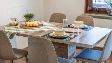 A dining area with a wooden table, four chairs, a checkered tablecloth, and a small plant.