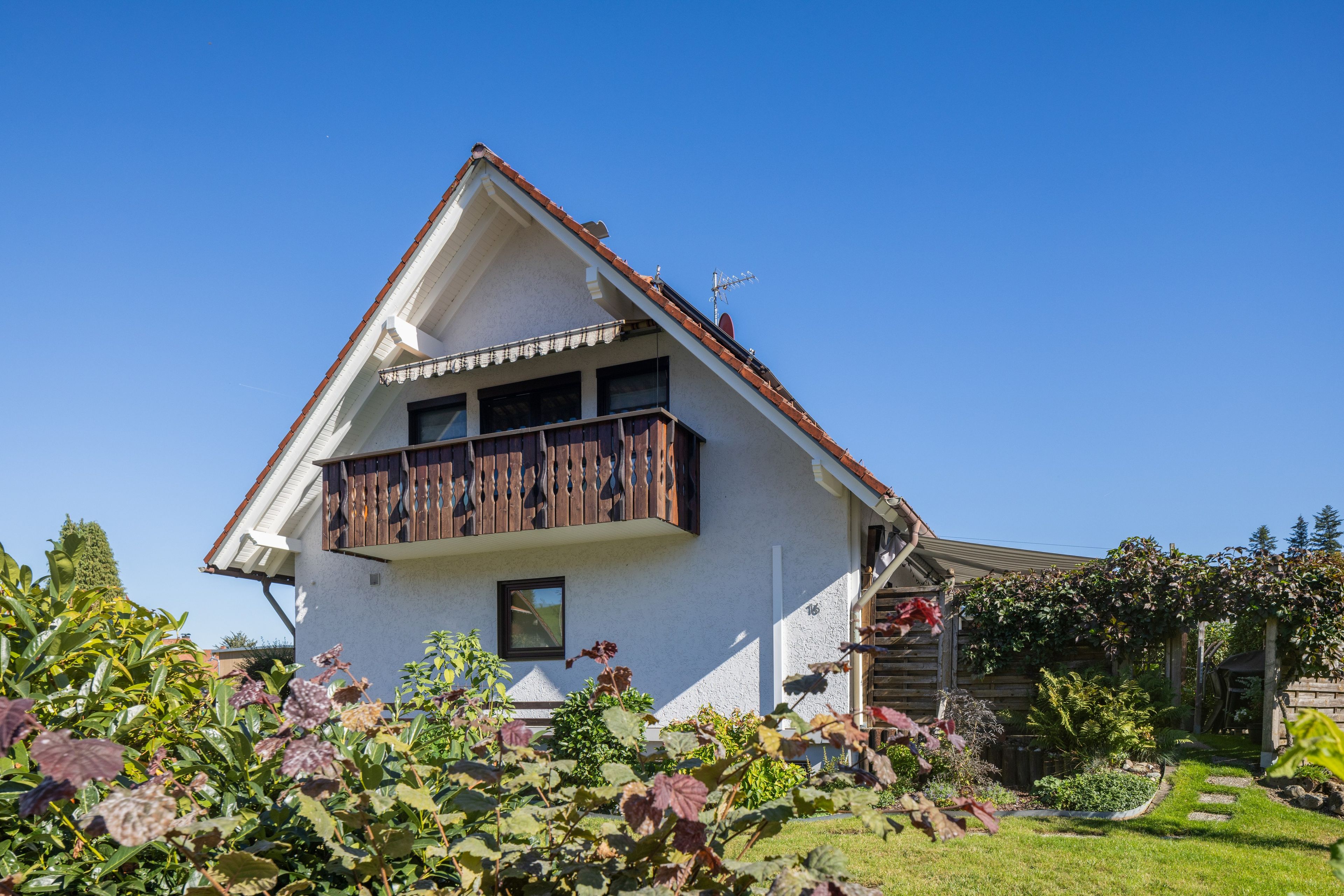 A two-story house with a balcony, surrounded by a garden.