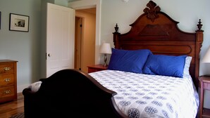 A bedroom with a wooden bed, a nightstand with a lamp, a dresser, and a door leading to another room. - 3-bedroom house on a peaceful street on the river in Waldoboro (Waldoboro)