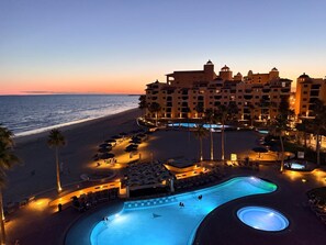 Un resort con piscina, playa y un edificio grande con múltiples balcones.