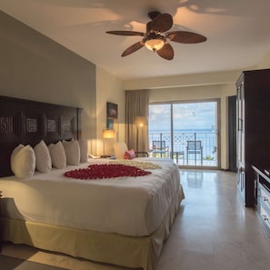Ein Hotelzimmer mit einem großen Bett, einem Deckenventilator, einem Balkon mit Meerblick und einem Schreibtisch mit Lampe.