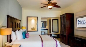 Ein Hotelzimmer mit einem Bett, einem Deckenventilator, einem Fernseher, einem Spiegel und einer Tür zu einem anderen Raum.