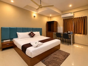 A modern hotel room with a large bed, a desk, a chair, a ceiling fan, and an air conditioning unit. - Hotel AD (Indore)