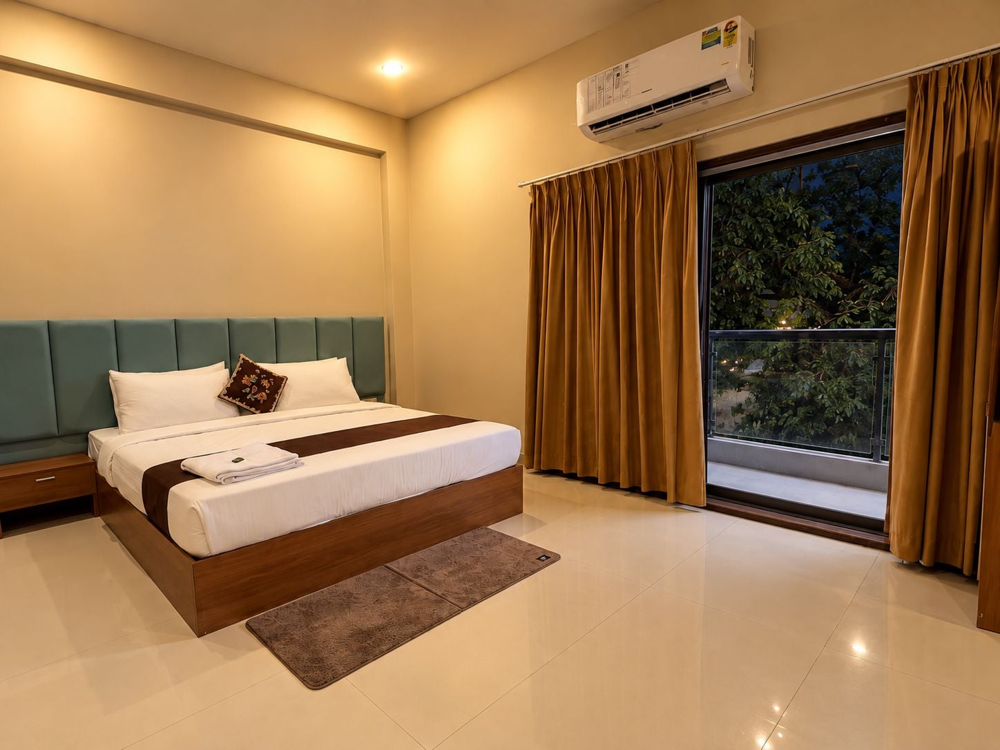 Una habitación de hotel con cama, mesita de noche, ventana con cortinas y un equipo de aire acondicionado.