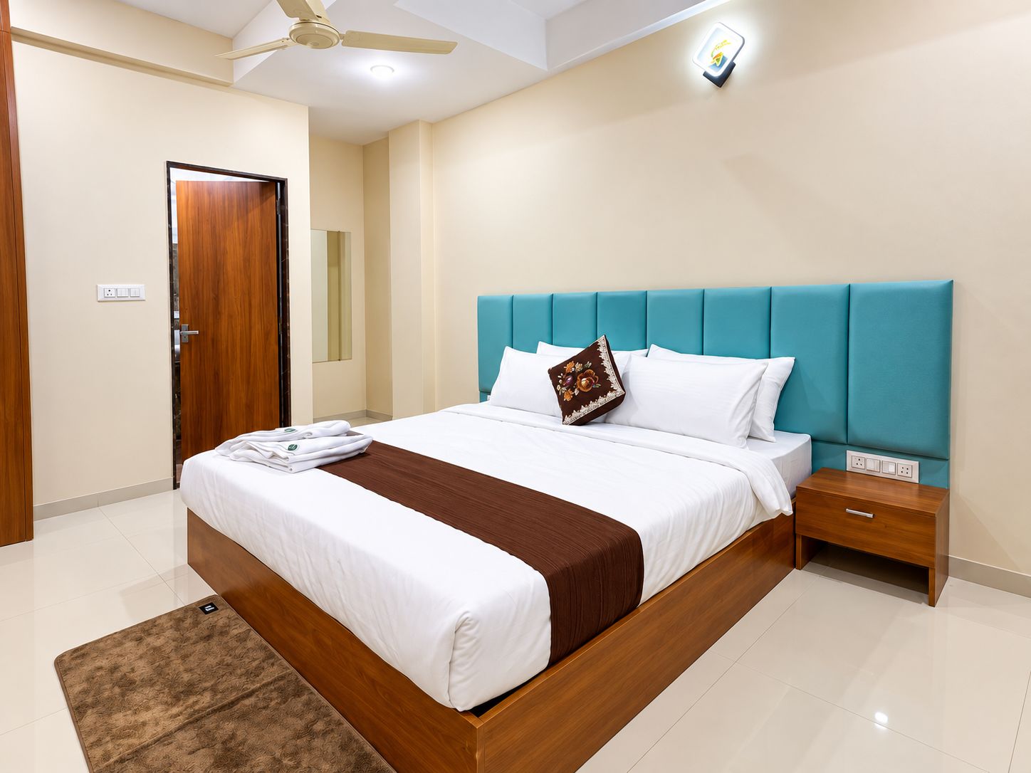 A hotel room with a bed, a nightstand, a ceiling fan, and a wall-mounted light.