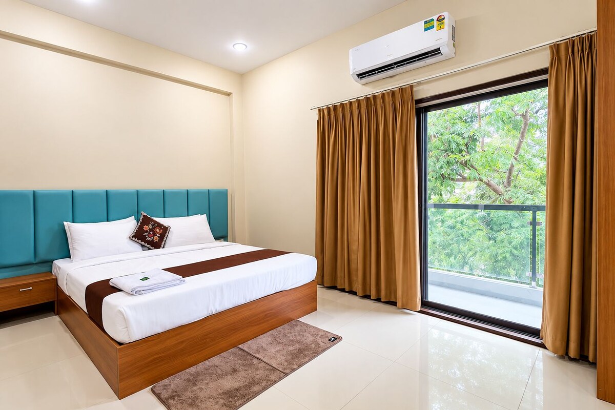 A hotel room with a bed, a nightstand, a window with curtains, and an air conditioning unit.