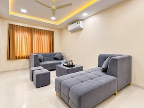 A modern living room with a grey sofa set, a coffee table, and a ceiling fan. - Hotel AD (Indore)