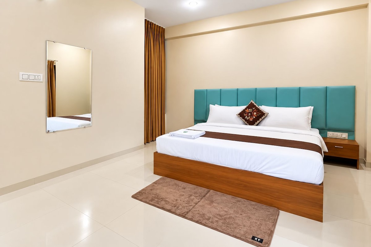 A hotel room with a bed, a nightstand, a mirror, and a wall-mounted light fixture.