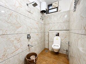 A bathroom with a toilet, shower, and a bucket. - Hotel AD (Indore)
