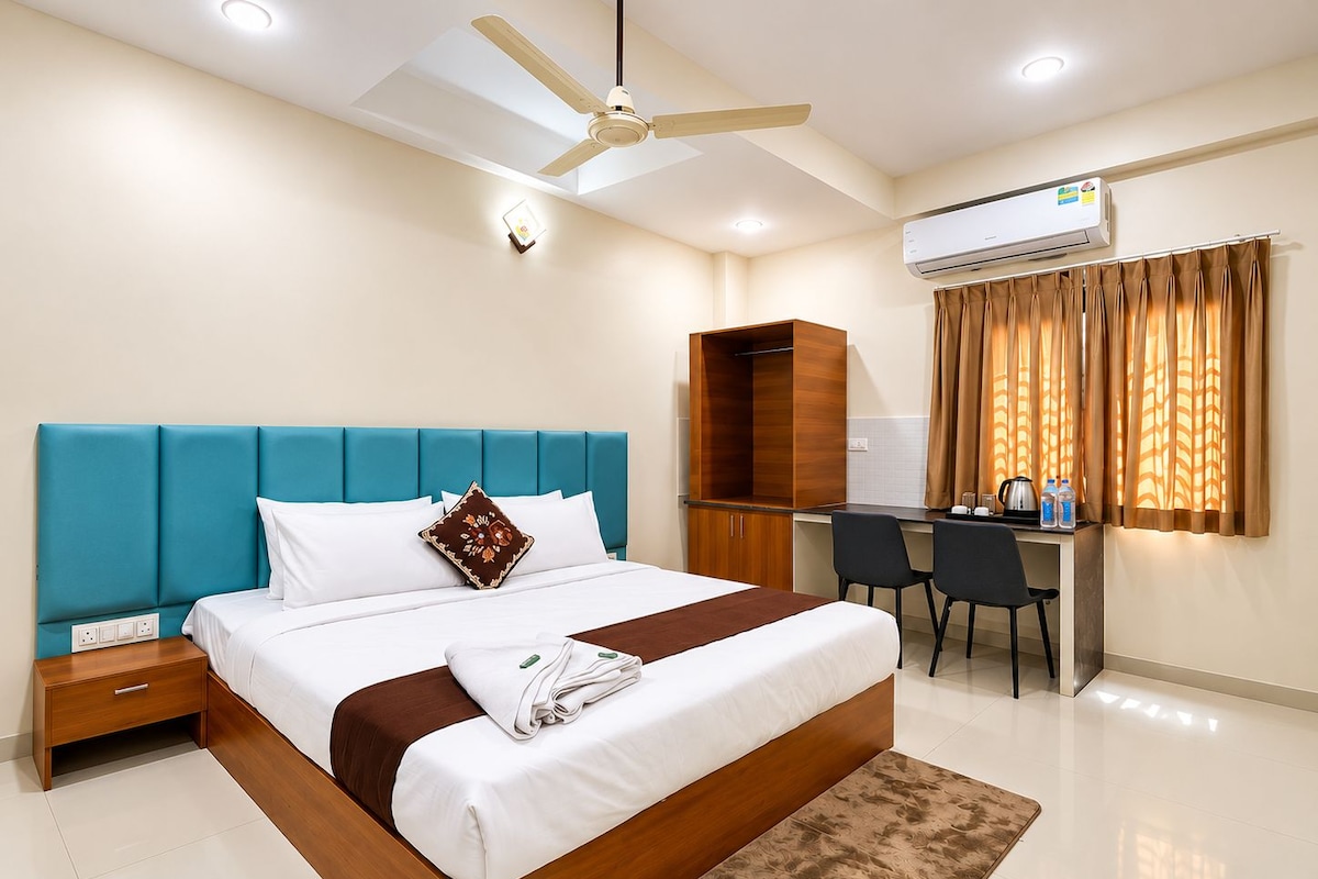 A hotel room with a bed, a desk, a chair, a wardrobe, a ceiling fan, and an air conditioning unit.