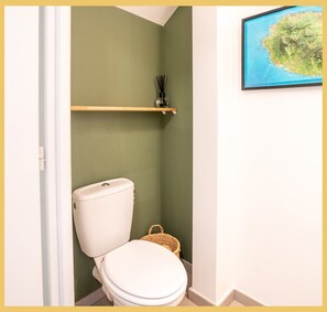 Ein kleines Badezimmer mit Toilette, einem Regal darüber und einer gerahmten Karte an der Wand.