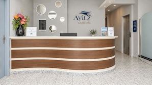 A hotel reception desk with a logo, a welcome sign, and a sign indicating the 1st floor. - Ayit Hotel (Rhodes)