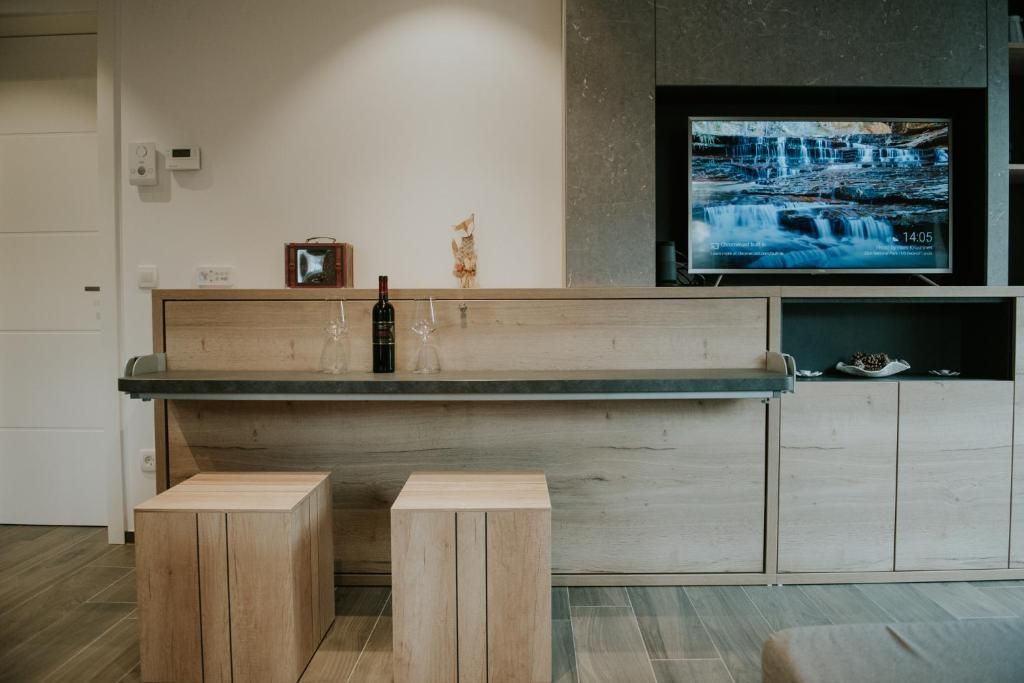 A modern living room with a wooden bench, two stools, a television mounted on a wall, and a shelf with items.