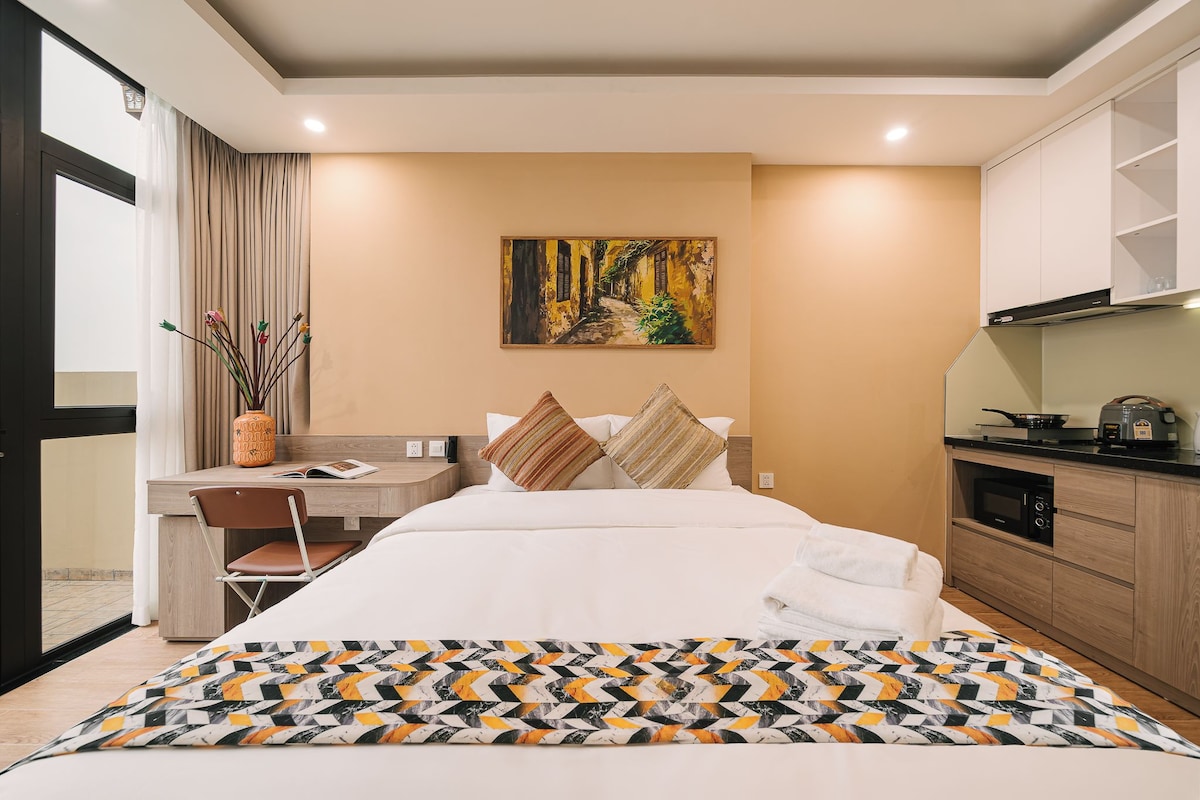 Une chambre d’hôtel avec un lit, un bureau, une chaise, un tableau au mur et une kitchenette.
