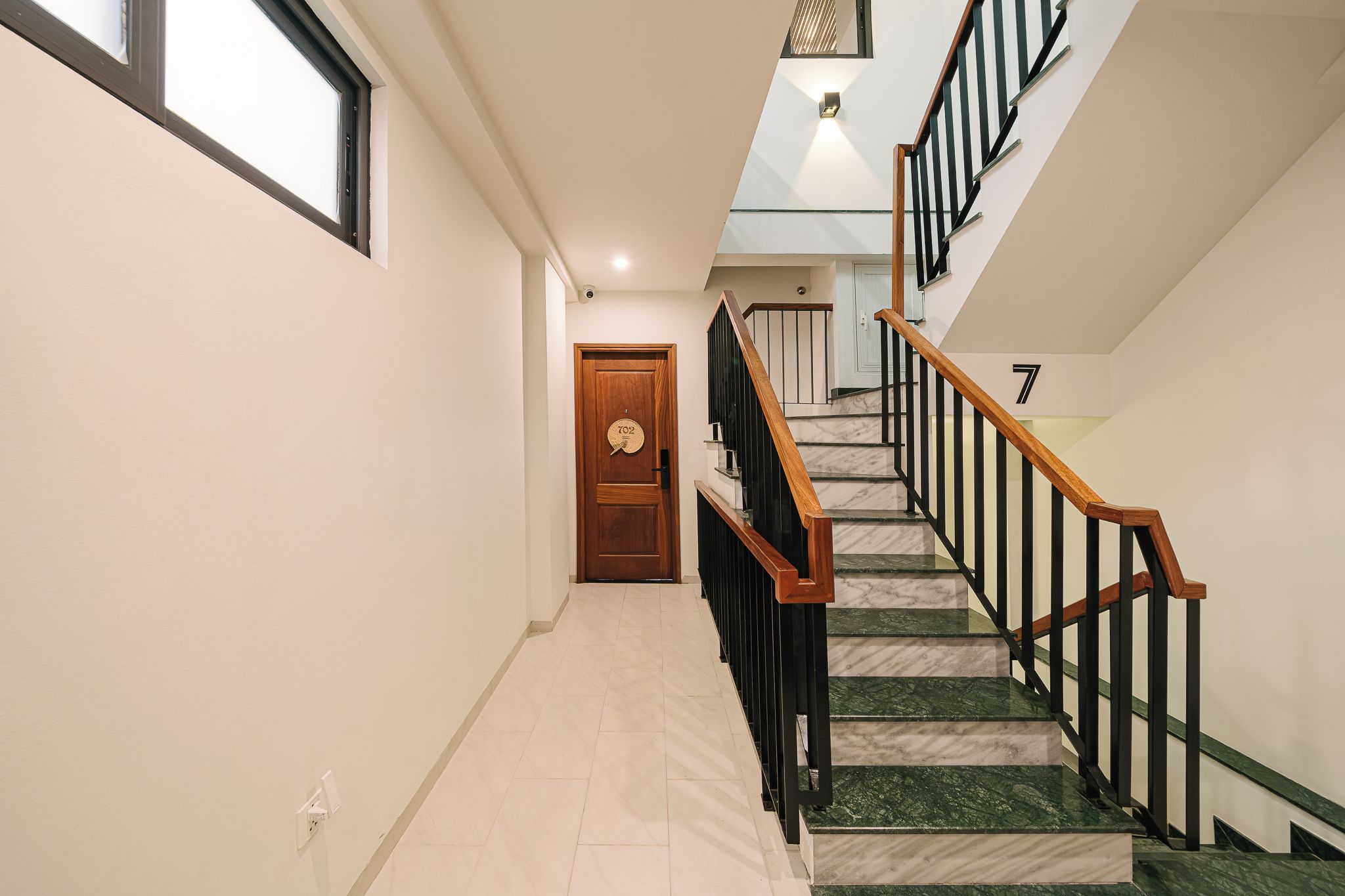 Un couloir avec une porte en bois, un escalier avec des rampes noires et le chiffre « 7 » peint sur le mur.