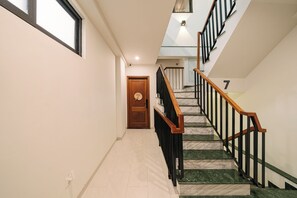 Un pasillo con una puerta de madera, una escalera con barandales negros y el número 7 en la pared.
